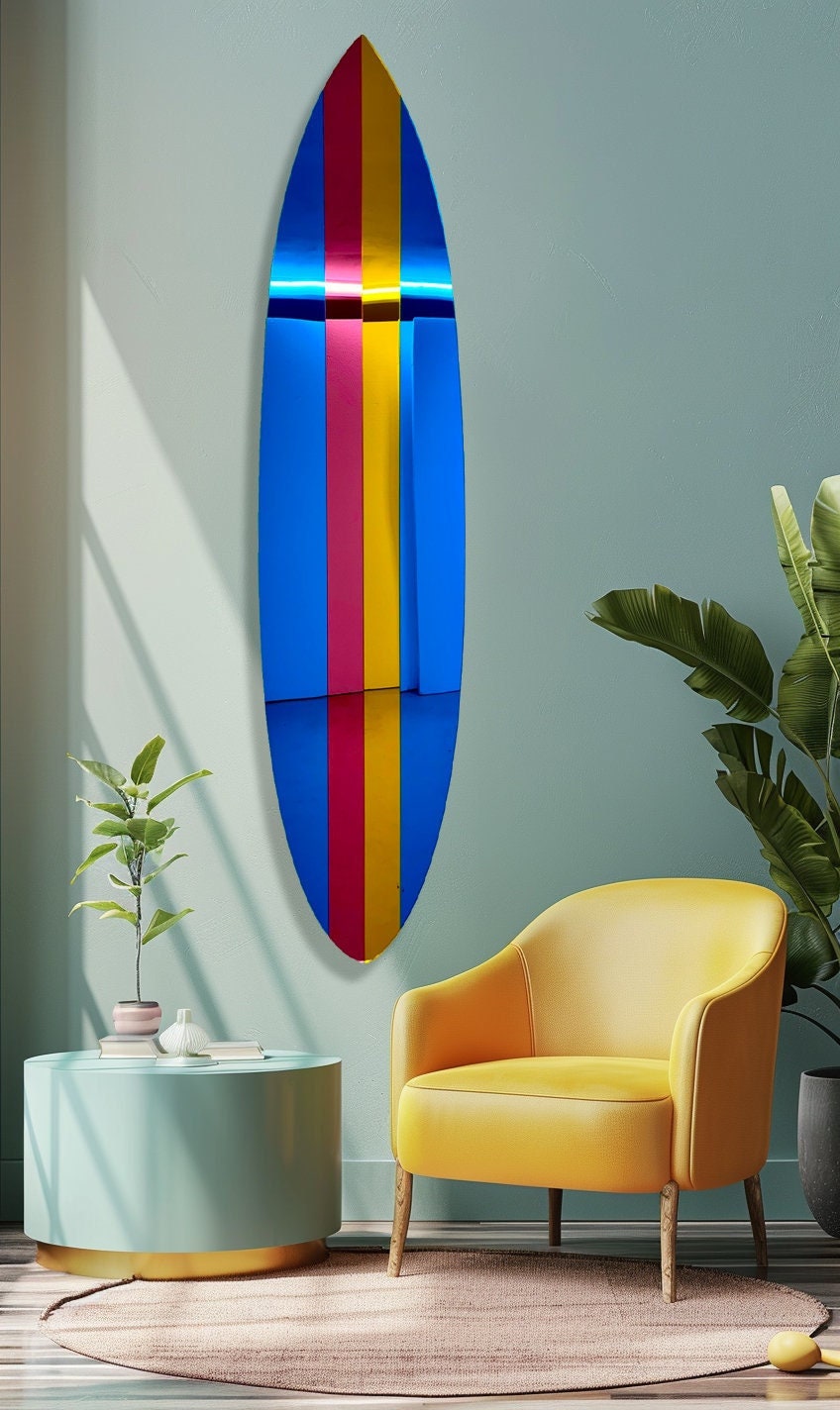 The uniQstiQ Retro Surfboard Wall Art—mirrored acrylic pop art with red, yellow, and blue vertical stripes—hangs on a pastel wall beside a yellow chair and plants.